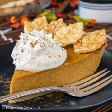 A black plate with a slice of pumpkin pie topped with whipped cream on it