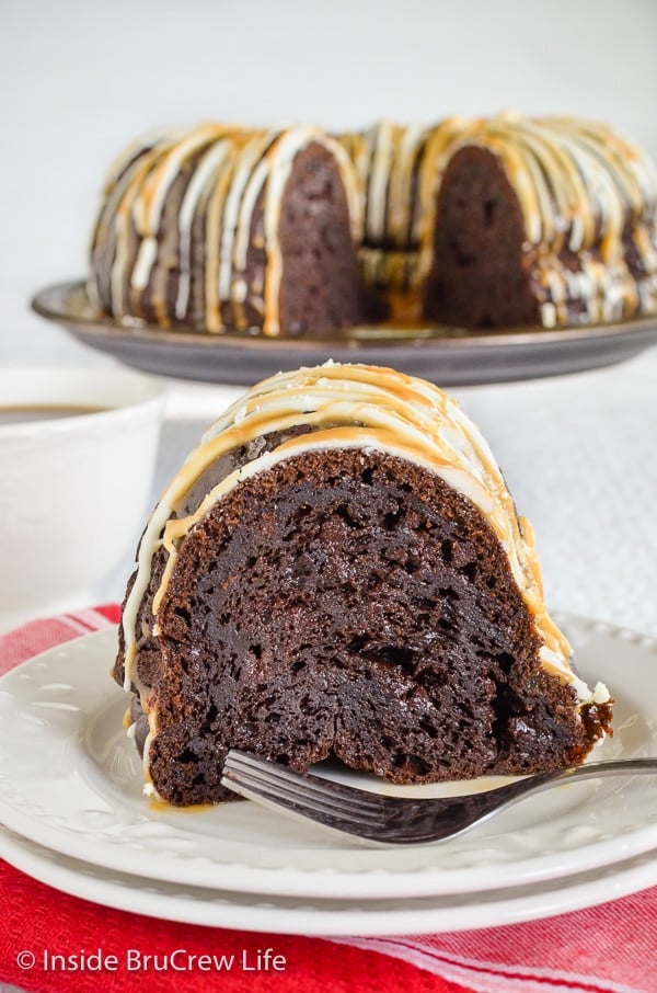 A white plate with a slice of salted caramel mocha bundt cake on it and cake plate with more cake behind it.