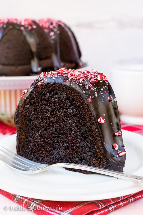 A white plate on a red towel with a slice of chocolate peppermint cake topped with chocolate and peppermint candies.