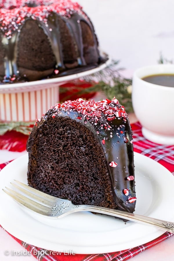 A white plate with a slice of peppermint bundt cake with chocolate glaze and peppermint bits on it.