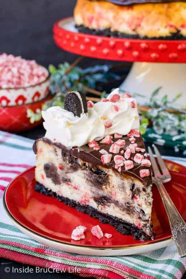 A slice of oreo cheesecake with peppermint bits and chocolate on a red plate.