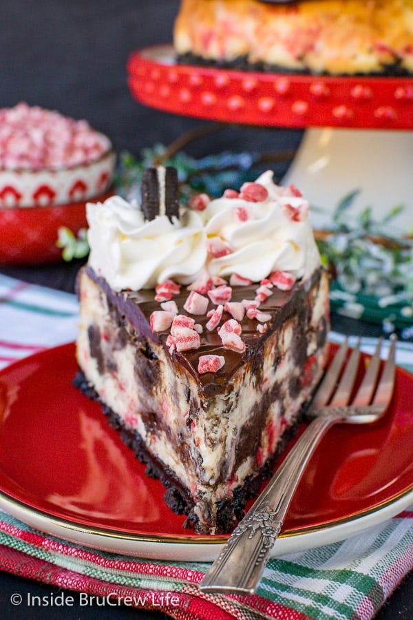 A slice of Peppermint Oreo Swirl Cheesecake on a red plate with a fork.