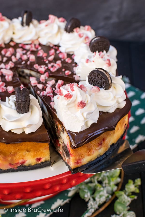 A slice of Peppermint Oreo Swirl Cheesecake being removed from a full size cheesecake.