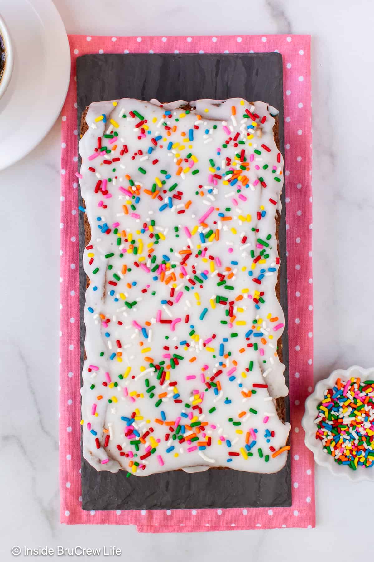 An overhead picture of a loaf of banana bread with glaze and sprinkles.