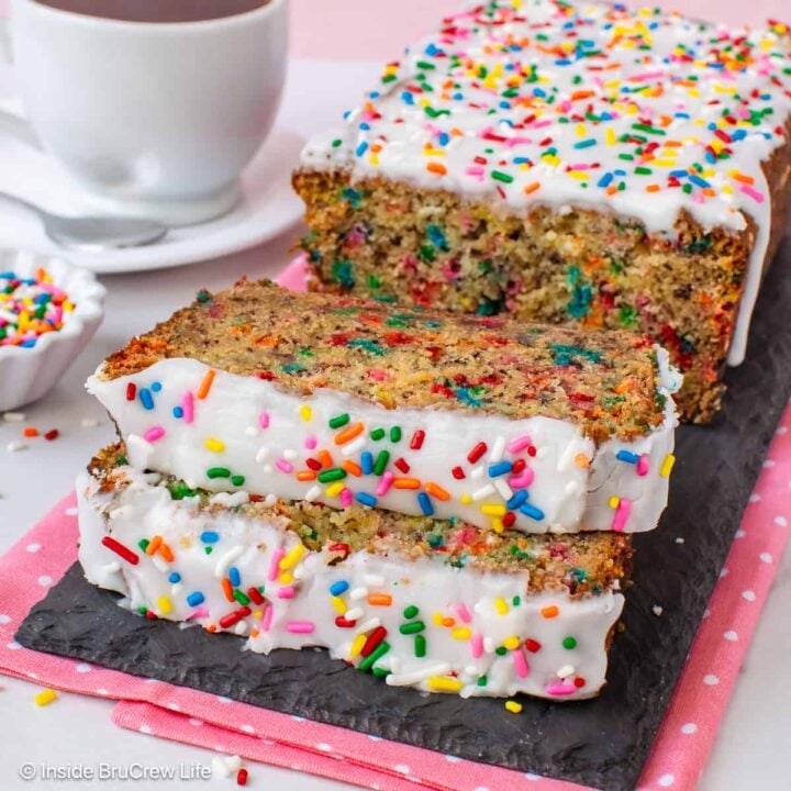 A loaf of birthday cake banana bread with two slices laying in front of it.