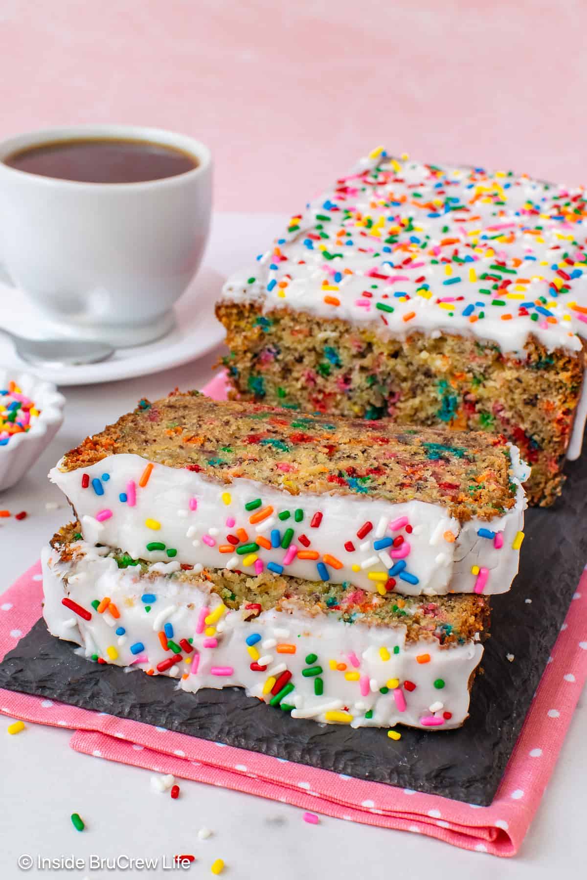 A loaf of birthday cake banana bread with two slices laying in front of it.