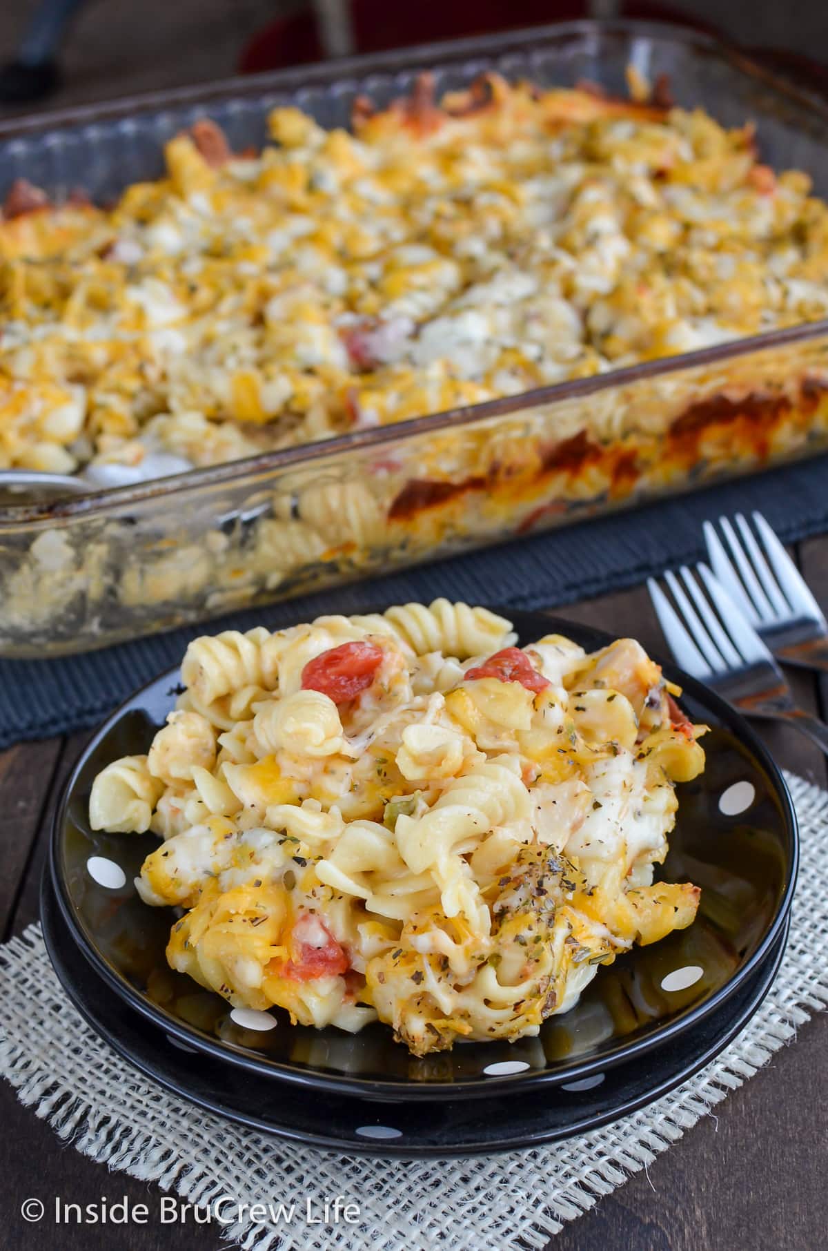 A black plate with a serving of baked pasta on it.