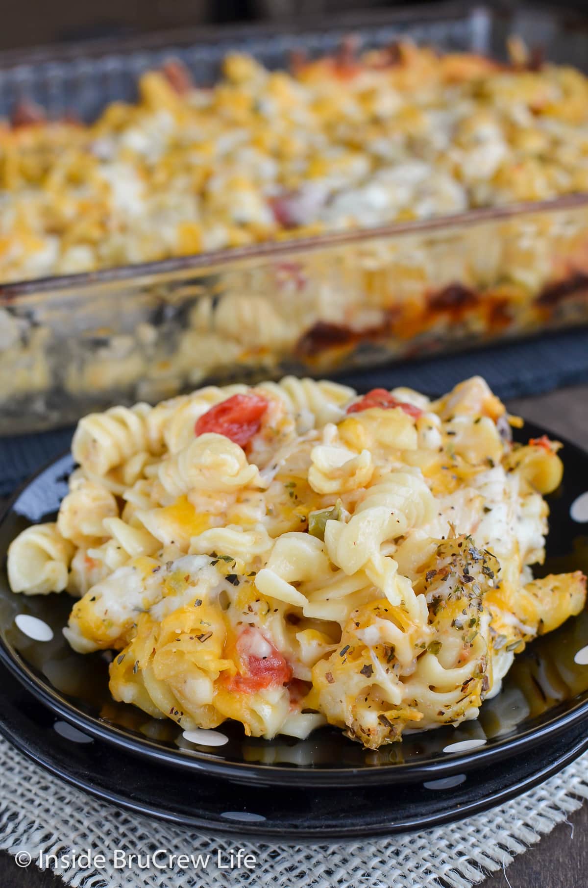 A black plate with a serving of baked cheesy pasta on it.