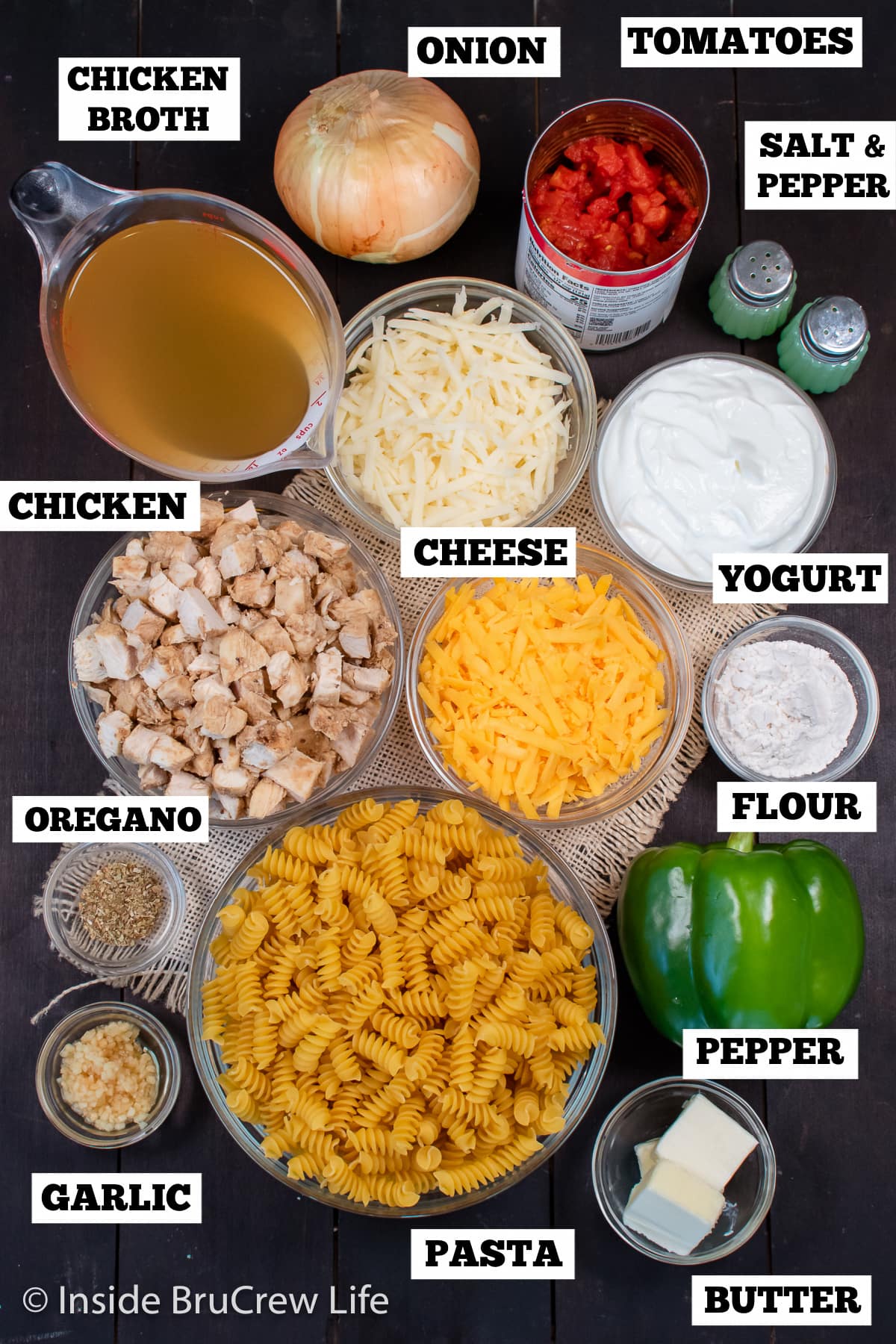 A brown board with bowls of ingredients needed to make a pasta casserole.