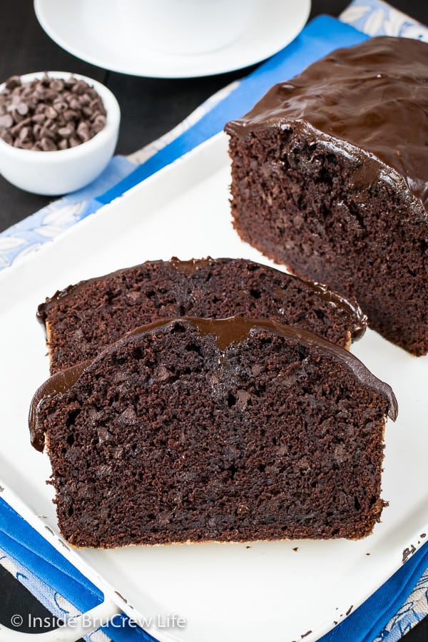 Two slices of chocolate banana bread with a loaf behind it on a white tray.