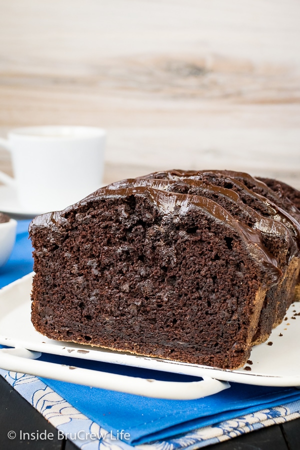 A white tray with slices of chocolate banana bread topped with frosting standing on it.