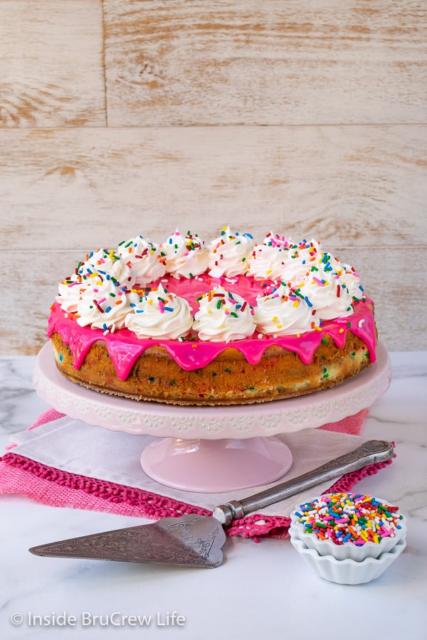 Funfetti Cheesecake - lots of sprinkles and a pink white chocolate glaze makes this cake batter cheesecake look and taste amazing. Great recipe to make for any celebration. #cheesecake #funfetti #cakebatter #sprinkles