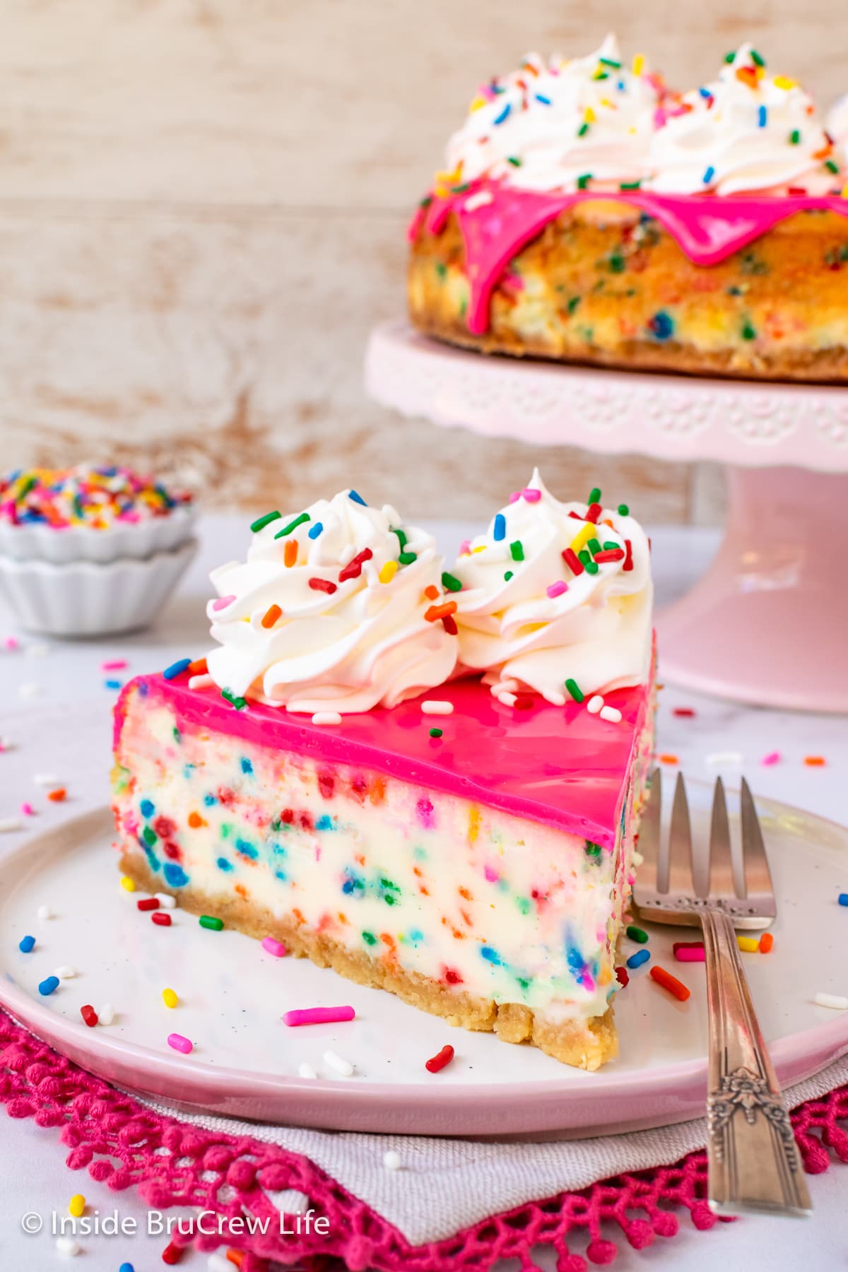 A slice of confetti cheesecake with pink chocolate on a plate.