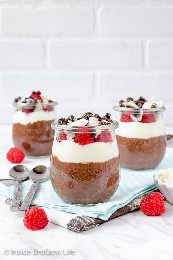 Three clear jars filled with a mocha chia seed pudding, coconut yogurt, raspberries, and coconut.