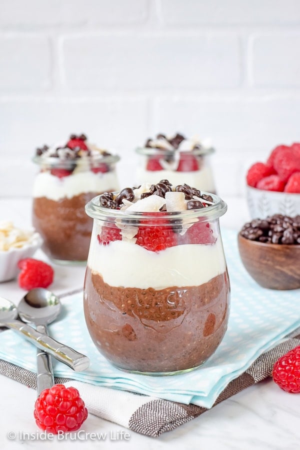 Three clear jars filled with mocha coconut chia seed pudding and topped with yogurt, raspberries, and coconut.