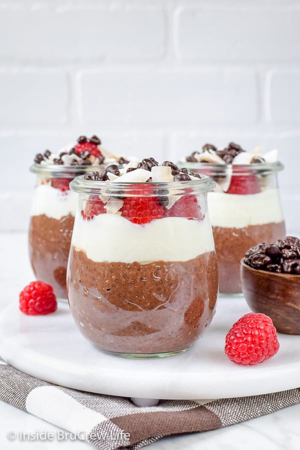 Three clear jars with mocha chia pudding, coconut yogurt, and raspberries in them.