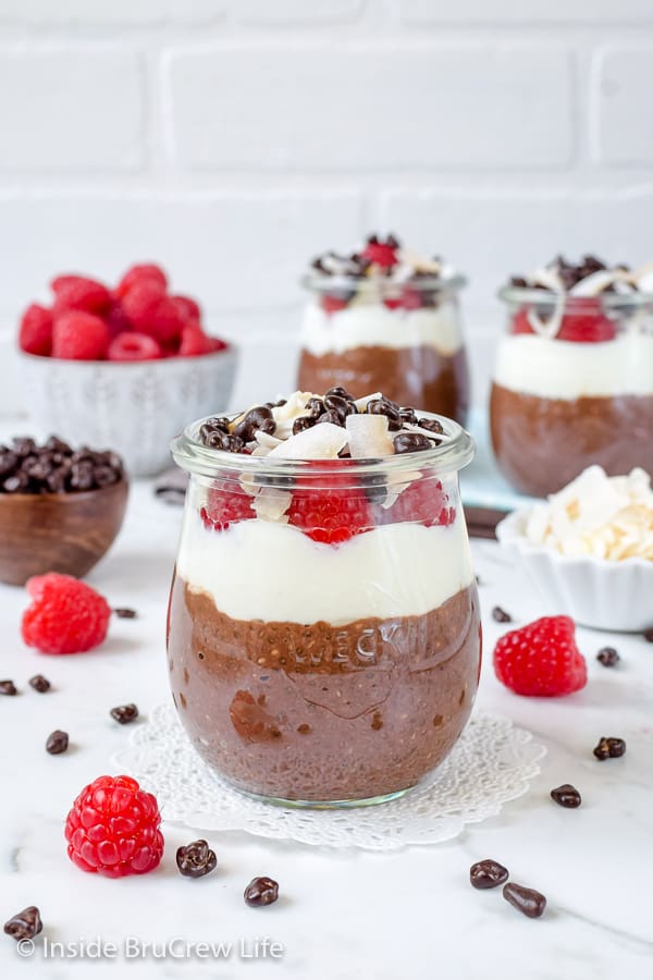 Jars filled with mocha coconut chia pudding and bowls with raspberries and coconut around them.