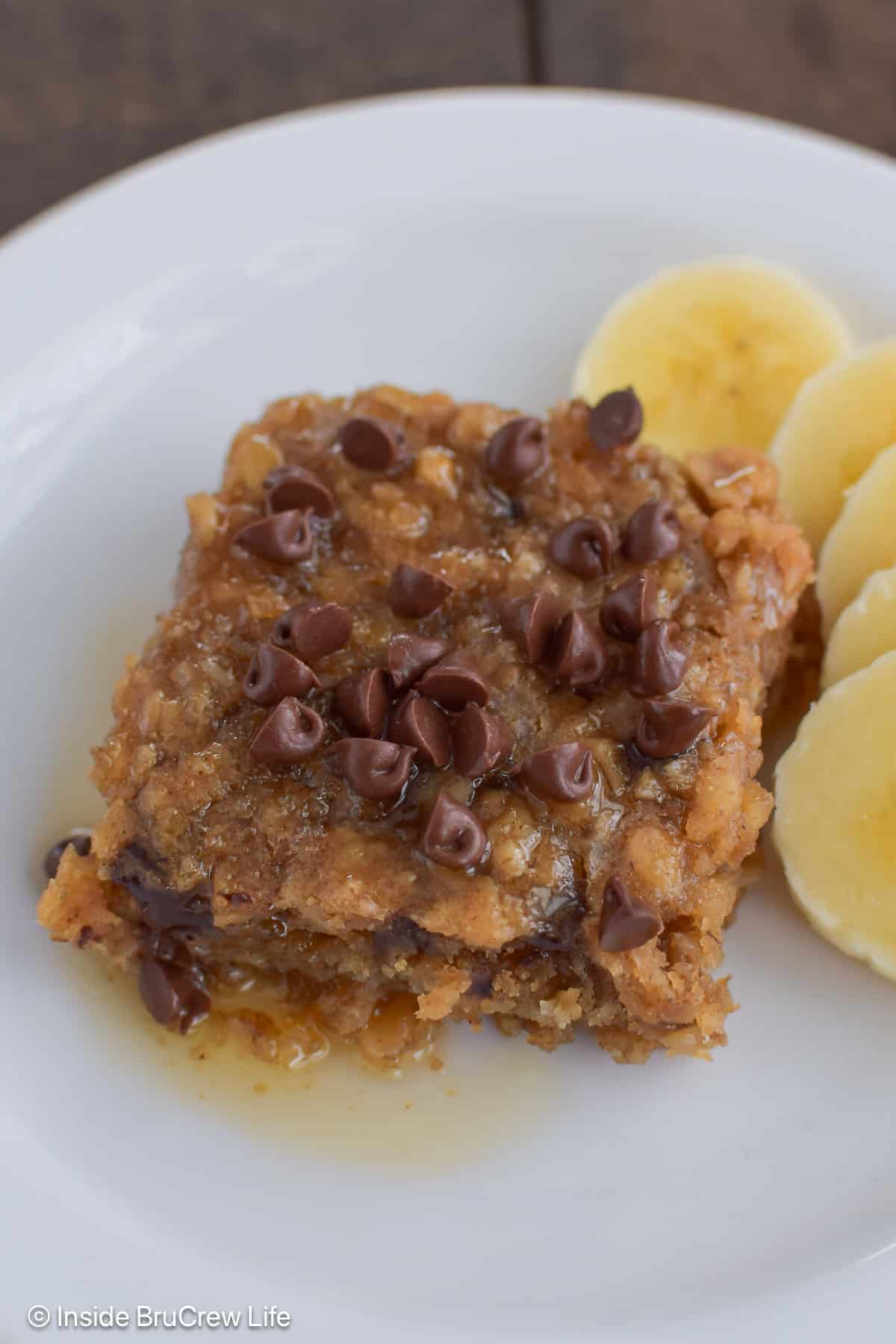 A piece of peanut butter baked oatmeal on a plate with chocolate chips and bananas.