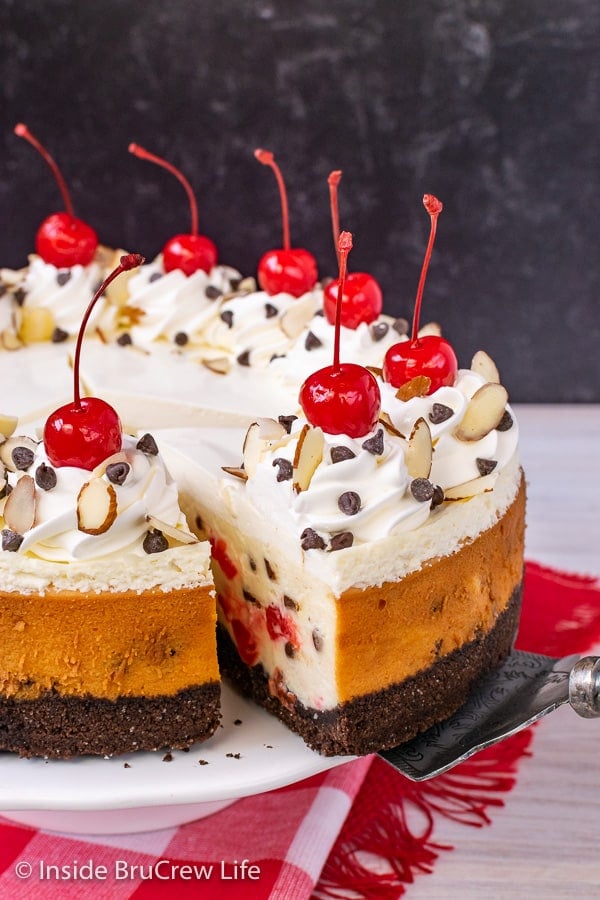 A full cheesecake with cherries and chocolate chips on a white cake plate.