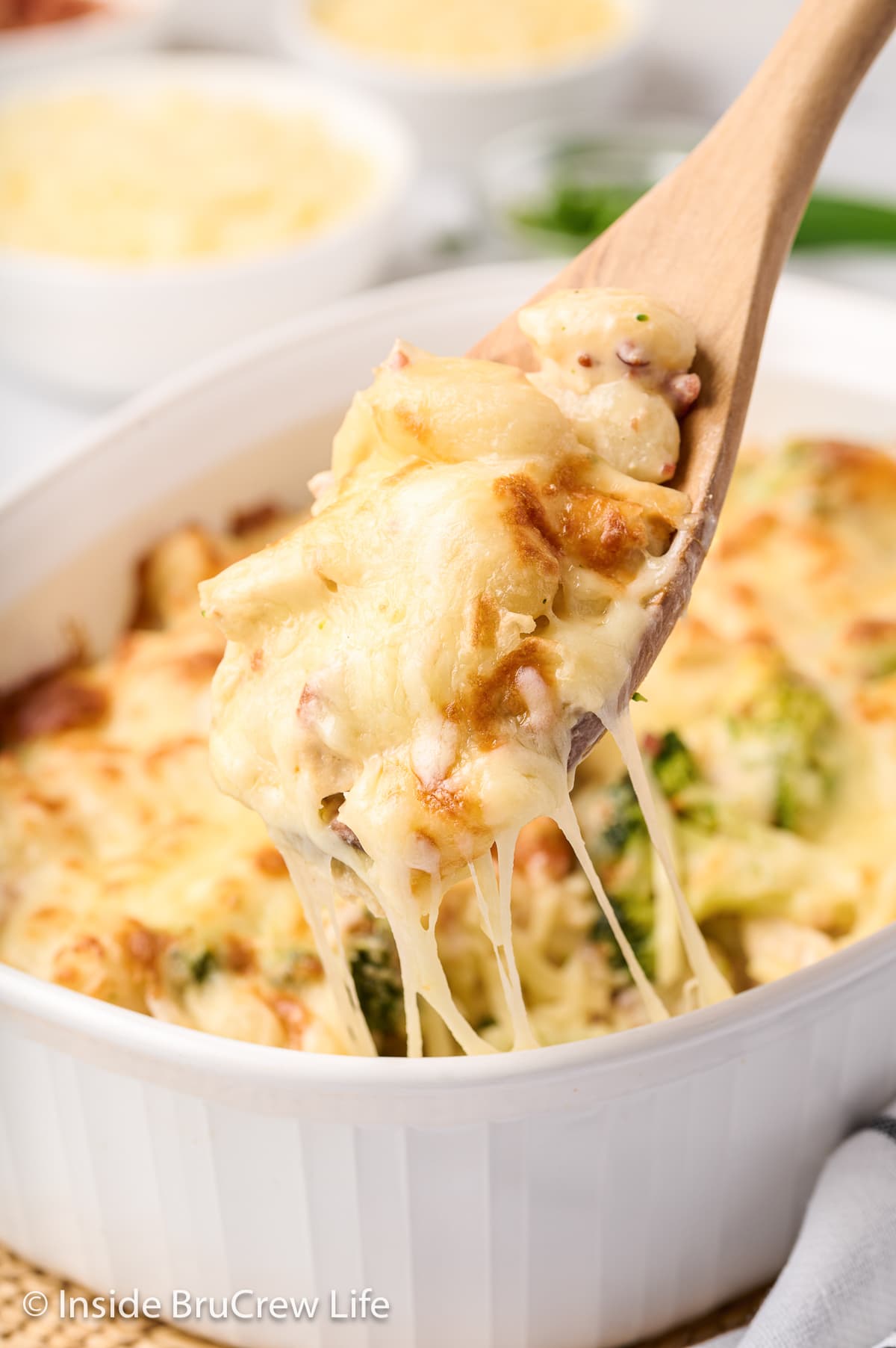 A spoon lifting a cheesy scoop of gnocchi bake out of a dish.