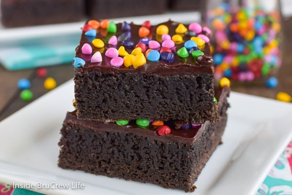 Two frosted brownies topped with rainbow chips on a white plate.