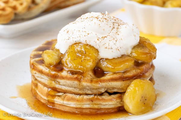 Two homemade banana waffles topped with caramelized bananas and whipped cream on a white plate