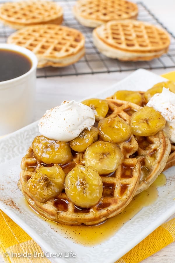 A stack of homemade banana waffles on a white plate topped with bananas and cool whip