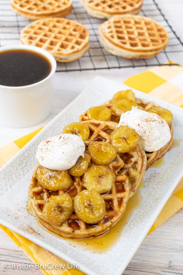 A white plate with four banana waffles topped with banana slices, Cool Whip, and cinnamon