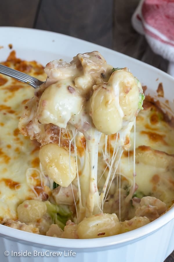 A spoon lifting up a cheesy bite of chicken alfredo gnocchi out of a white dish