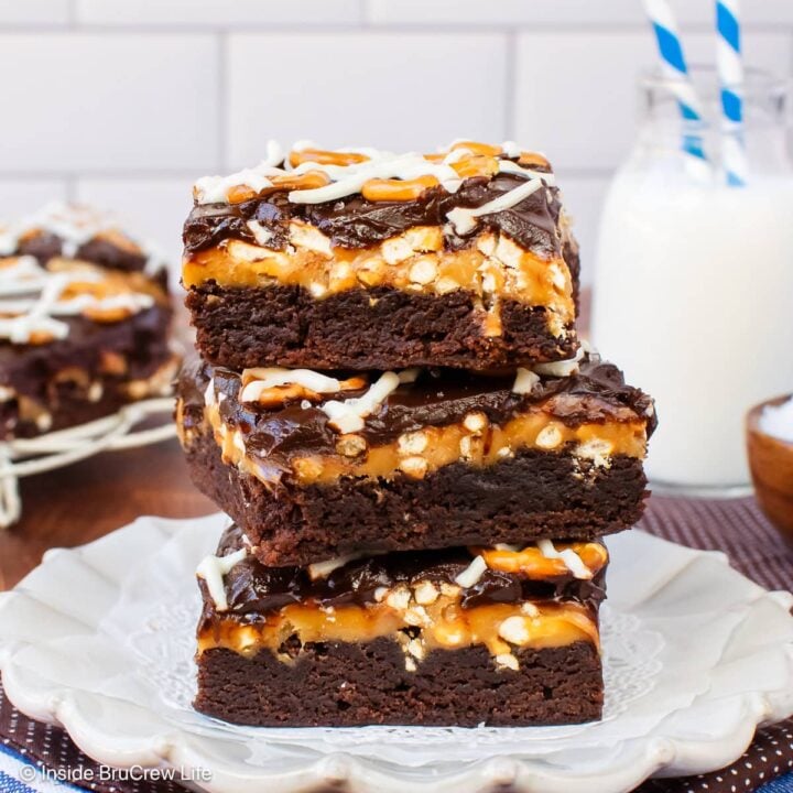 Three brownies with caramel, pretzels, and chocolate on a white plate.