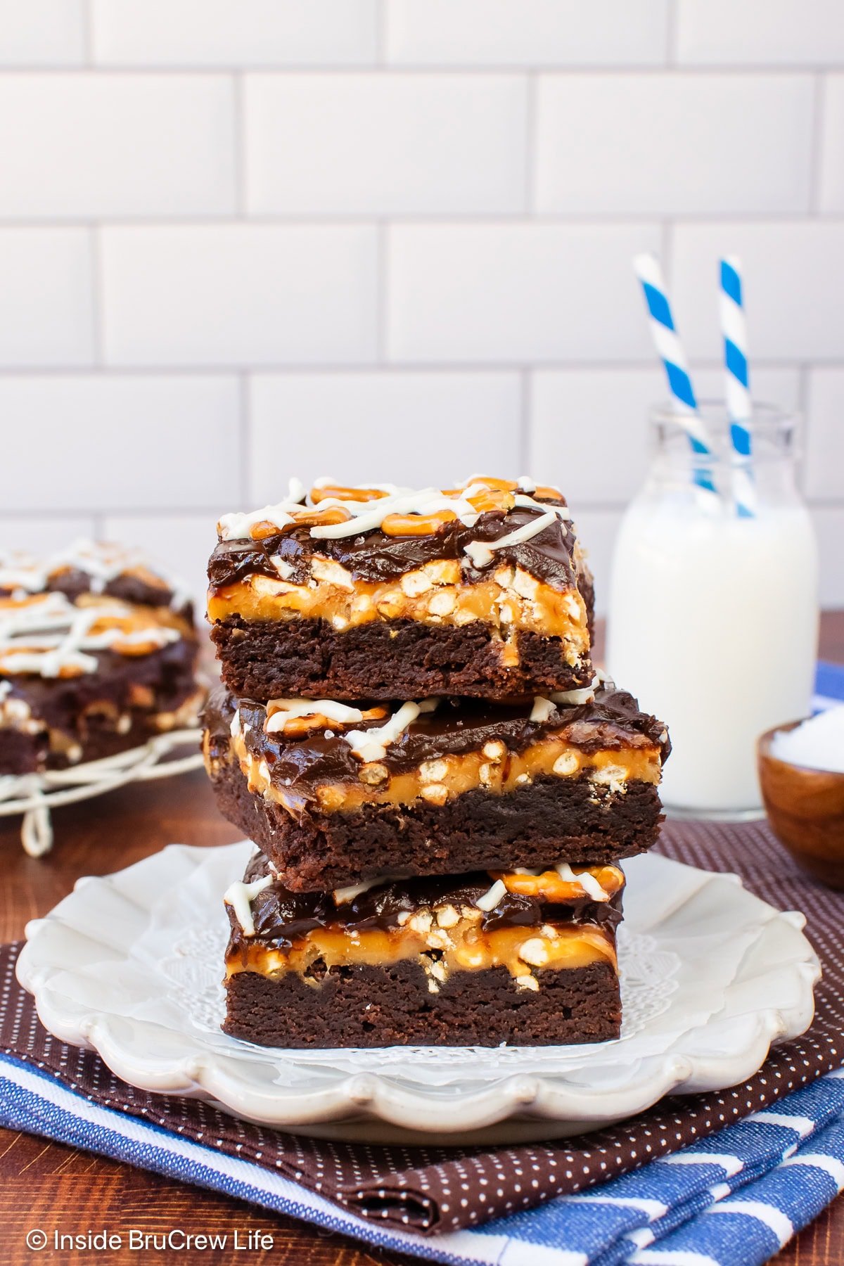 Three brownies with caramel, pretzels, and chocolate on a white plate.