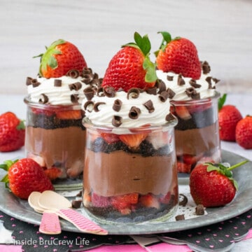 Three clear jars of strawberry chocolate cheesecake parfaits on a metal tray