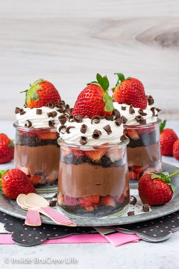 Three clear jars of chocolate cheesecake parfaits topped with Cool Whip and a strawberry.