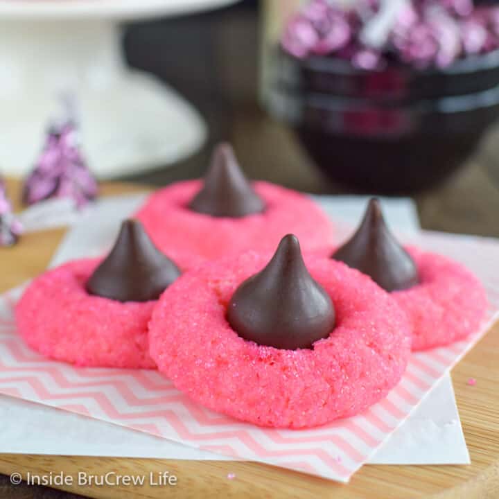 Pink cookies with kisses on top stacked on a board.