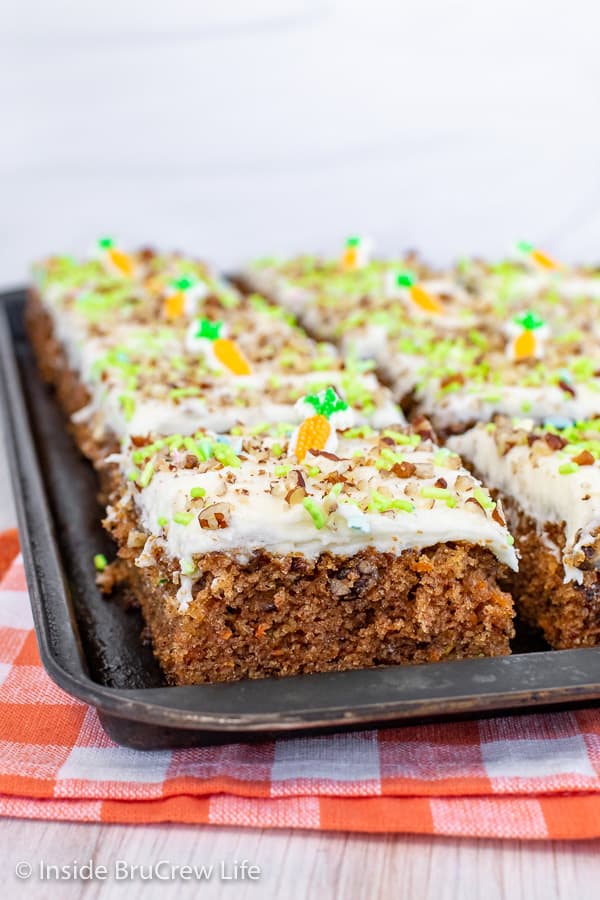 A close up picture of squares of carrot cake bars on a black sheet pan.