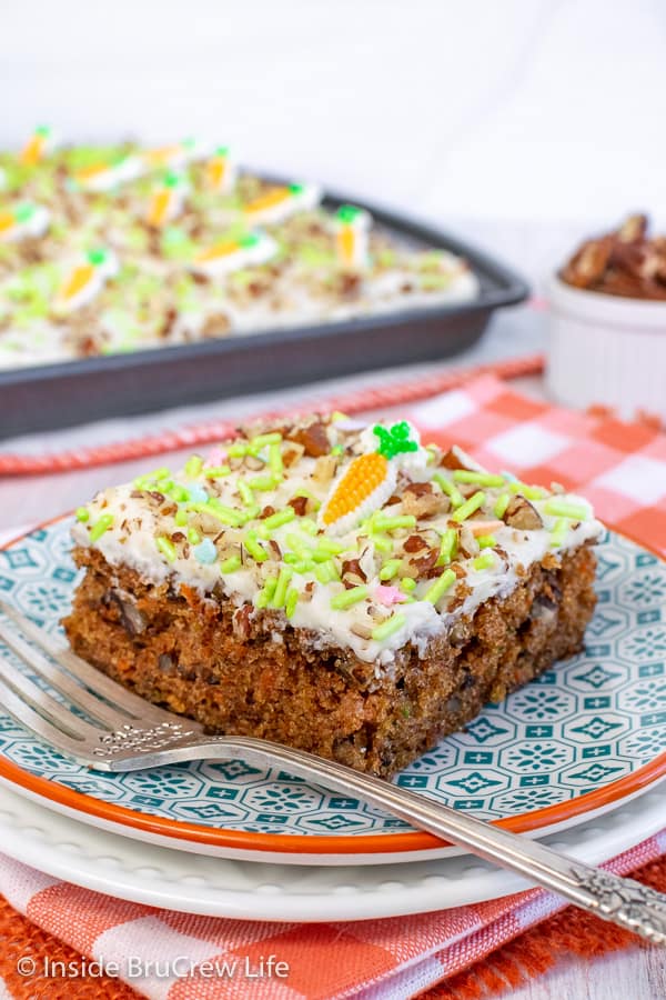 One square of carrot cake bars on a white and teal plate with a sheet pan in the background