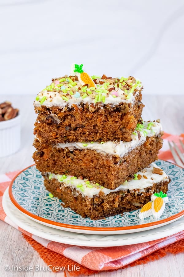 A stack of three carrot cake bars with cream cheese frosting on a white and teal plate.