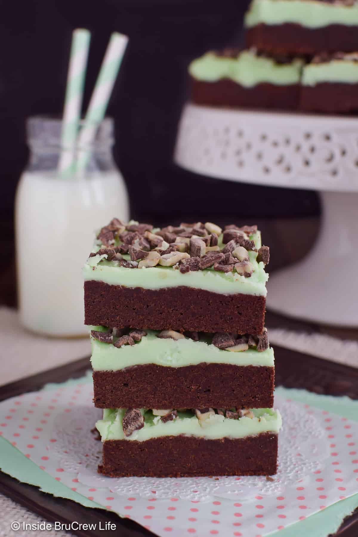 A stack of three chocolate cookie bars with mint frosting and chips stacked on a white paper.