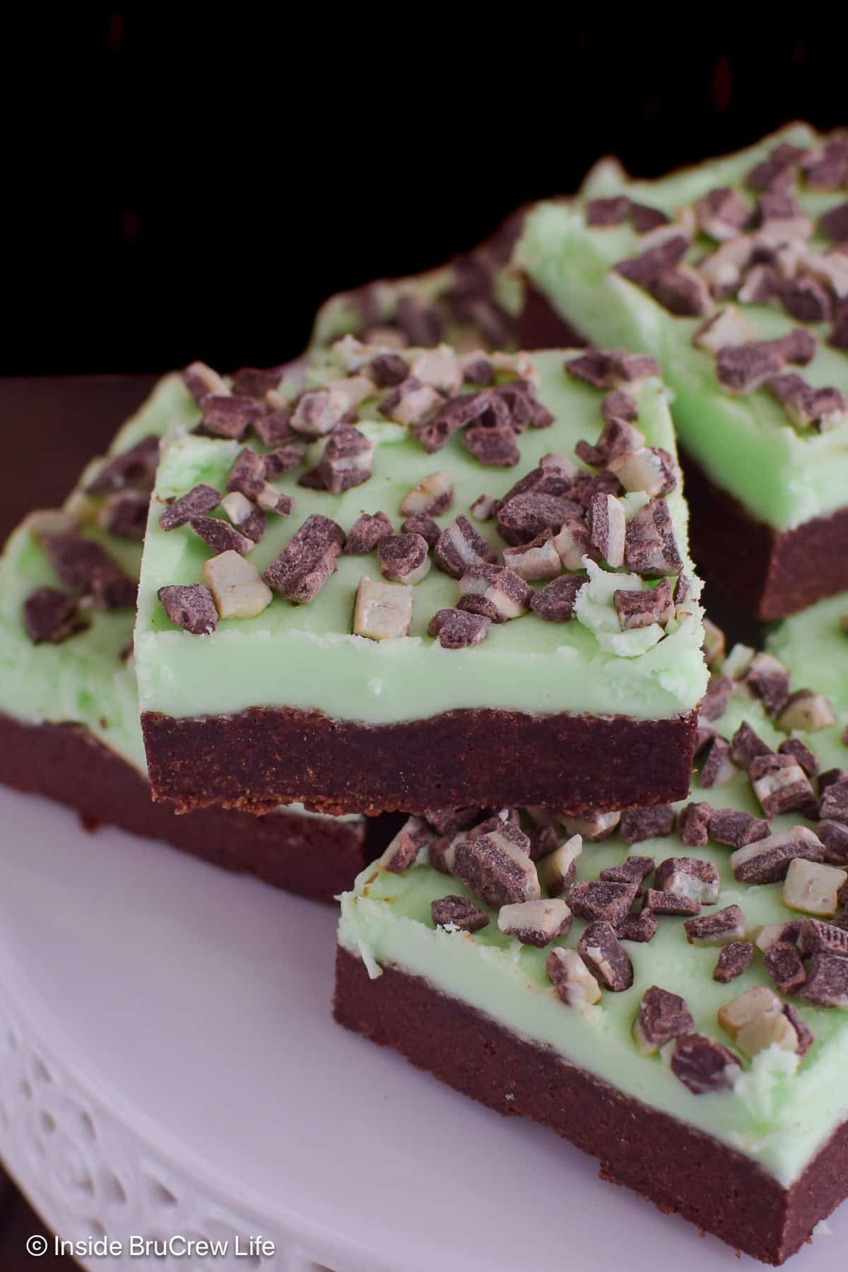 A stack of mint frosted cookie bars on a white cake plate.