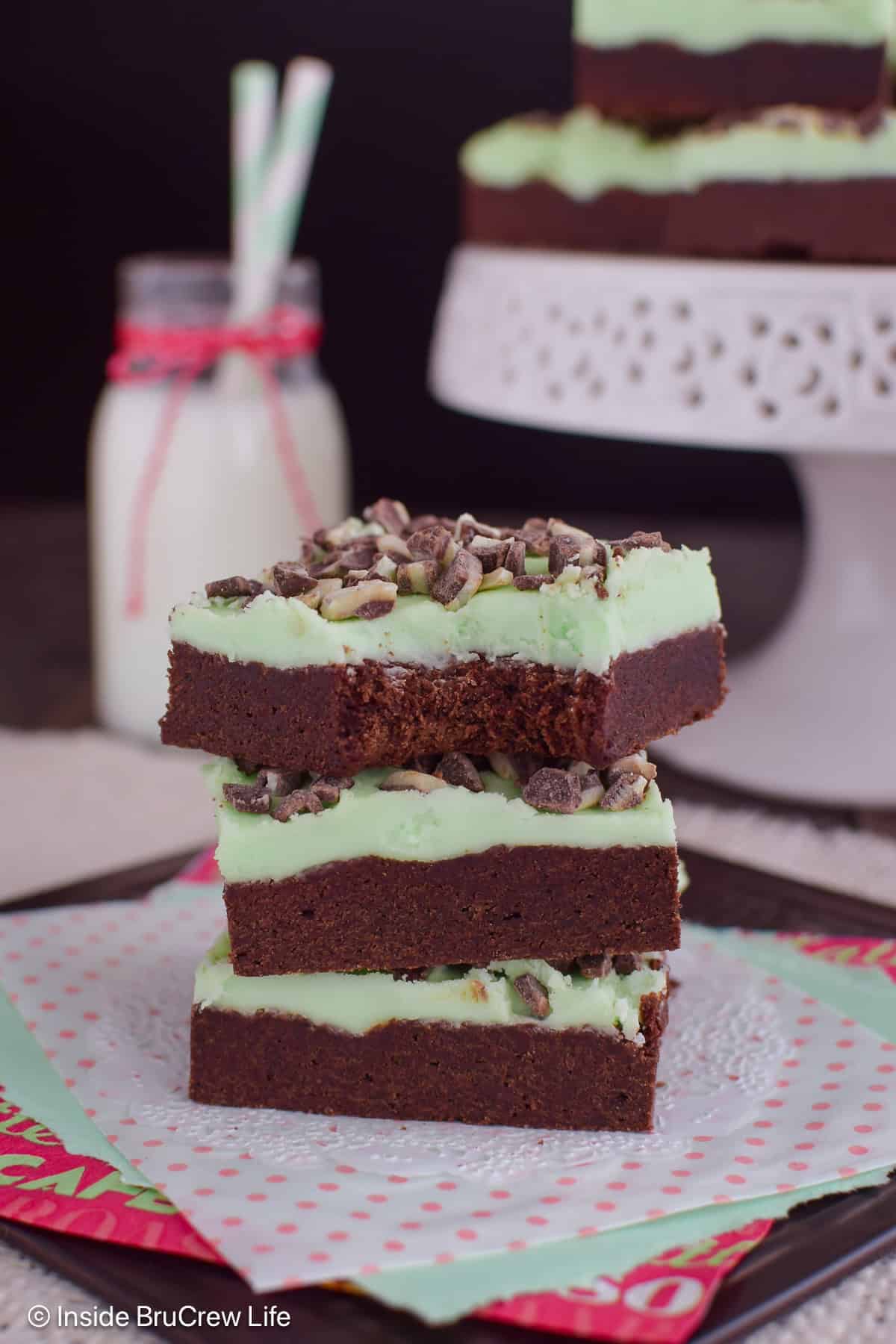 A stack of three frosted chocolate mint cookie bars with a bite out of the top one.