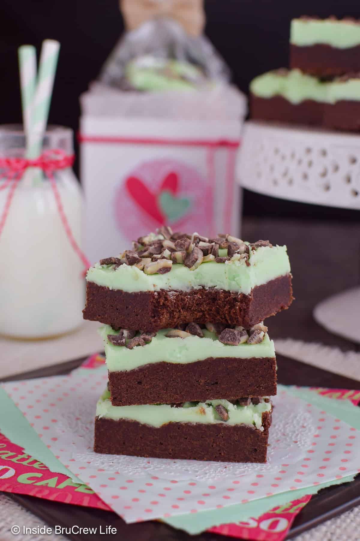 A stack of three frosted chocolate mint cookie bars with a bite out of the top one.