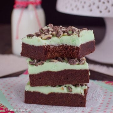 A stack of three frosted chocolate mint cookie bars with a bite out of the top one.