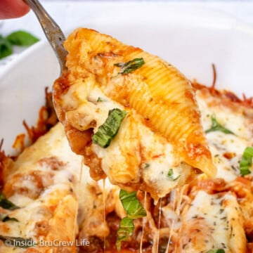 A white dish with stuffed shells in it and spoon lifting one up.