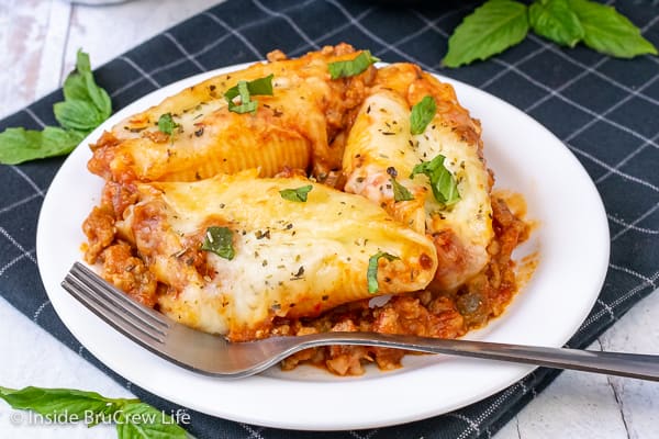 A white plate with a fork and three stuffed shells on it.