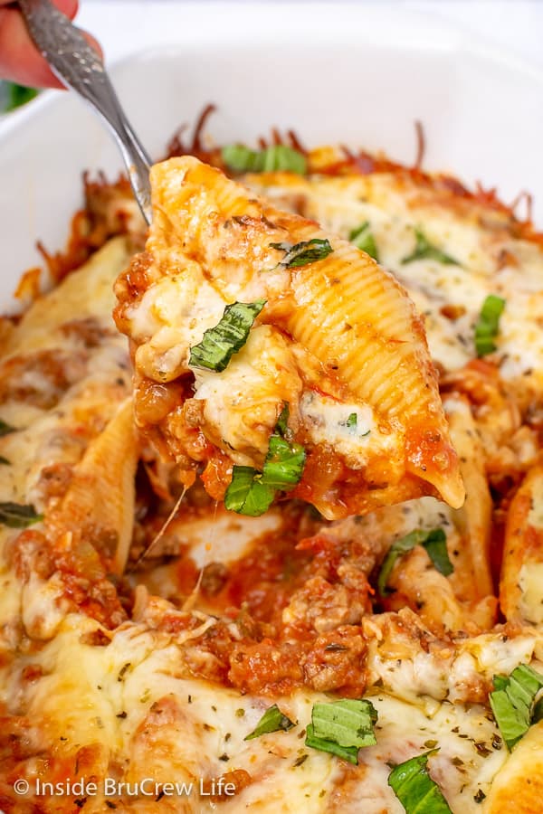 A pan of stuffed shells with a spoon lifting on shell up and out.