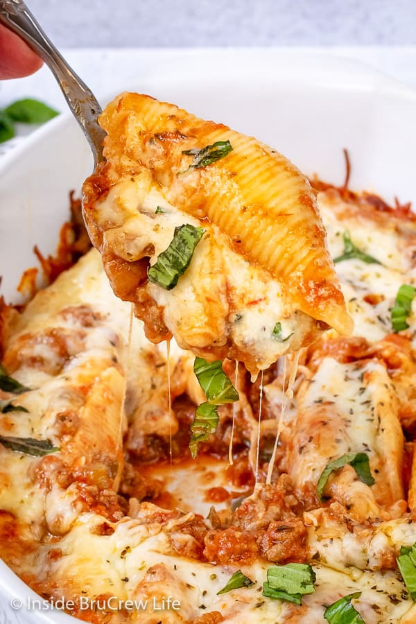 A white dish filled with stuffed shells and a meat sauce and spoon lifting out one stuffed shell.