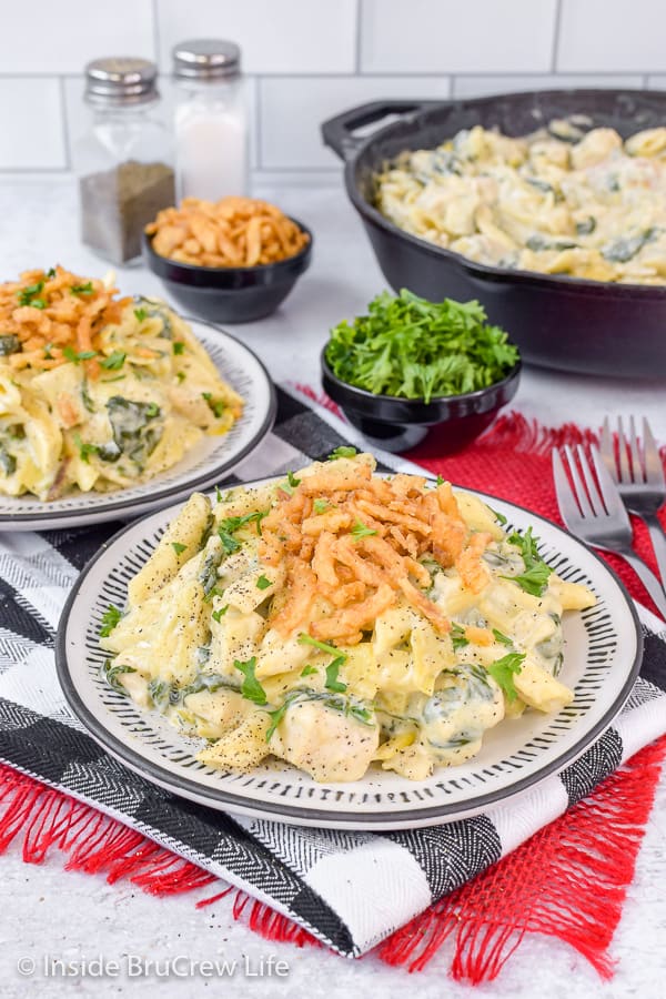 A white plate with chicken pasta on it with another plate and skillet in the background