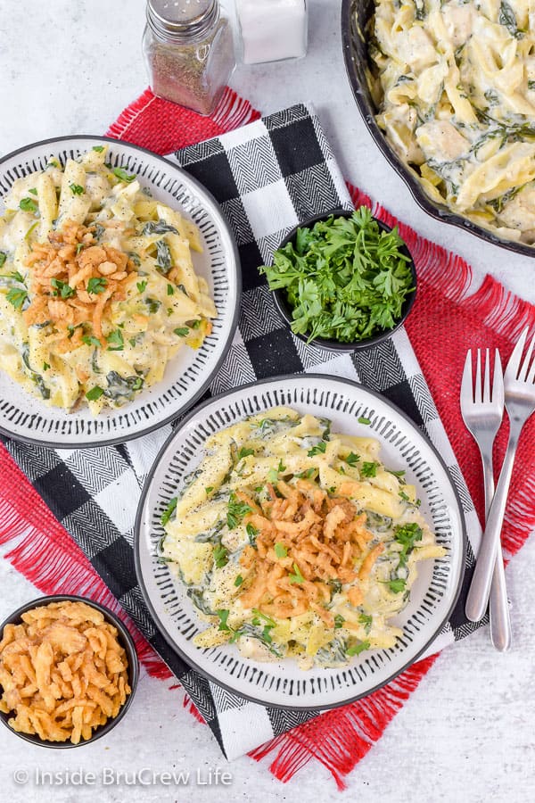 Overhead picture of two white plates of creamy chicken pasta with bowls of parsley and fried onions on the side