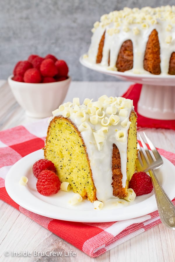 A white plate on a red and white checkered towel with a slice of lemon bundt cake on it