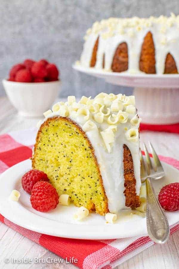 A slice of lemon bundt cake on a white plate with fresh raspberries around it